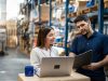 Warehouse manager and worker collaborating on laptop for efficient operations