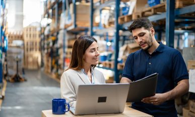 Warehouse manager and worker collaborating on laptop for efficient operations