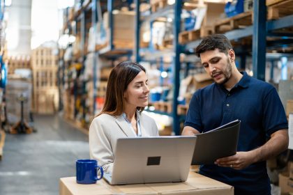 Warehouse manager and worker collaborating on laptop for efficient operations