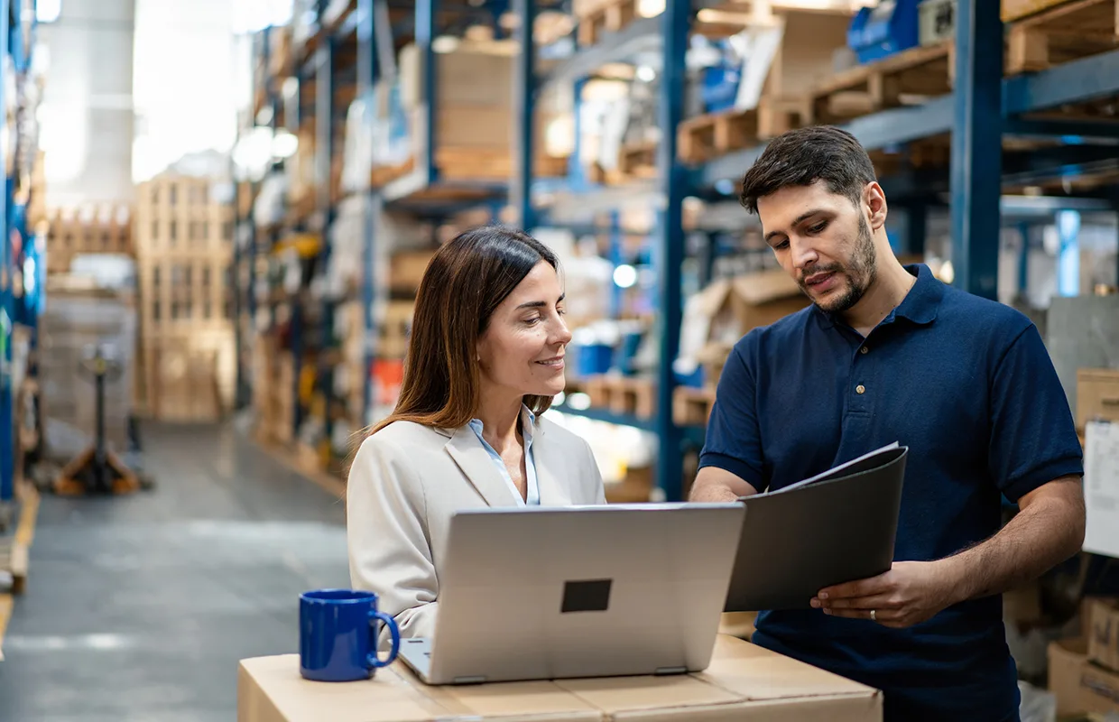 Warehouse manager and worker collaborating on laptop for efficient operations