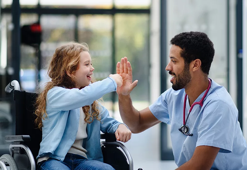 Young doctor having fun with little girl in wheelchair.