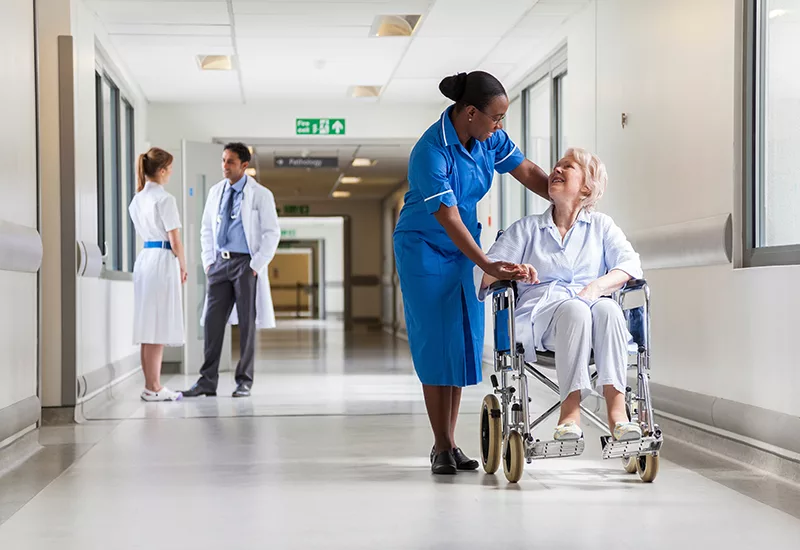 Senior Female Patient in Wheelchair & Nurse in Hospital